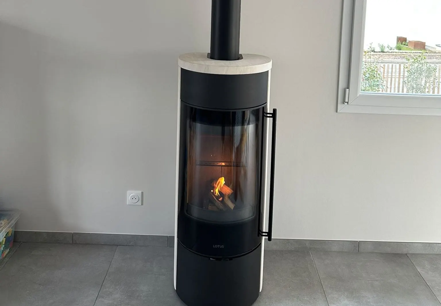 Poêle à bois Lotus allumé, installé par Eco Chauffage Lorraine dans un séjour clair