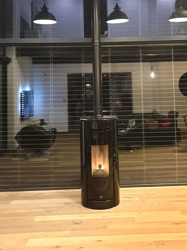 Poêle à granulés rond noir allumé au centre d'un loft au parquet clair