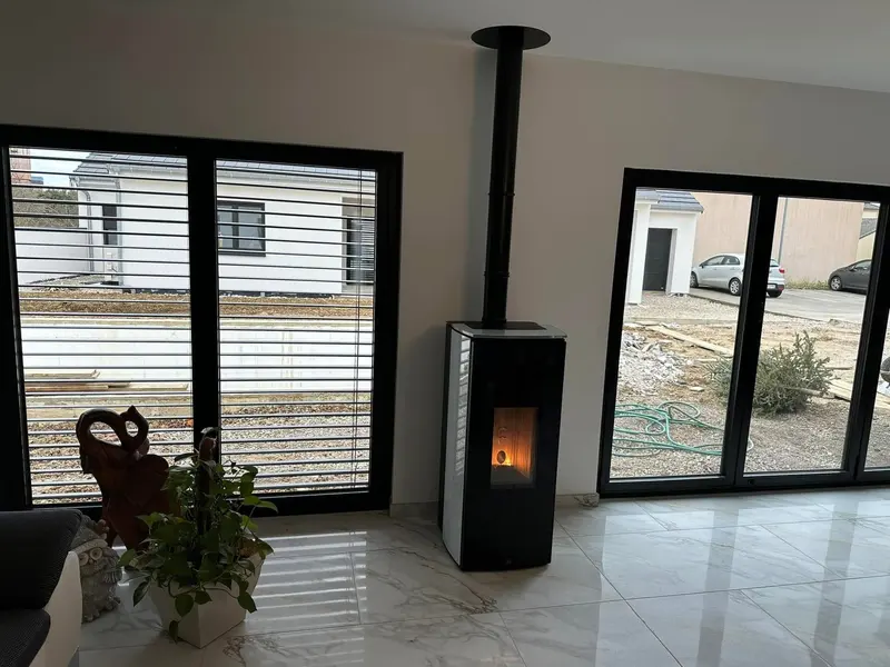 Vue large d'un séjour de maison neuve avec poêle à granulés et conduit vertical entre deux baies