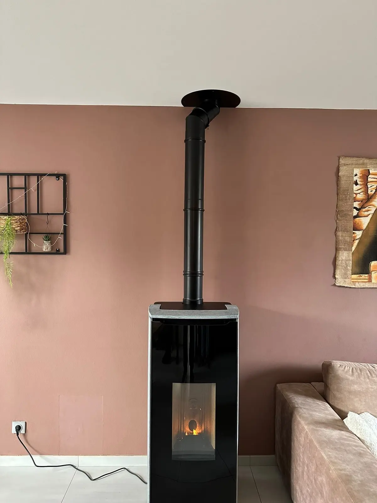 Poêle à granulés haut et étroit avec conduit vertical devant un mur rose poudré