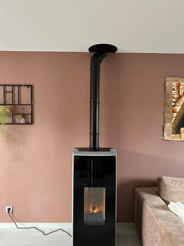 Poêle à granulés haut et étroit avec conduit vertical devant un mur rose poudré