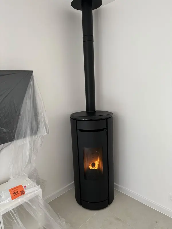 Poêle à granulés rond noir allumé dans l'angle d'une pièce, mobilier encore protégé