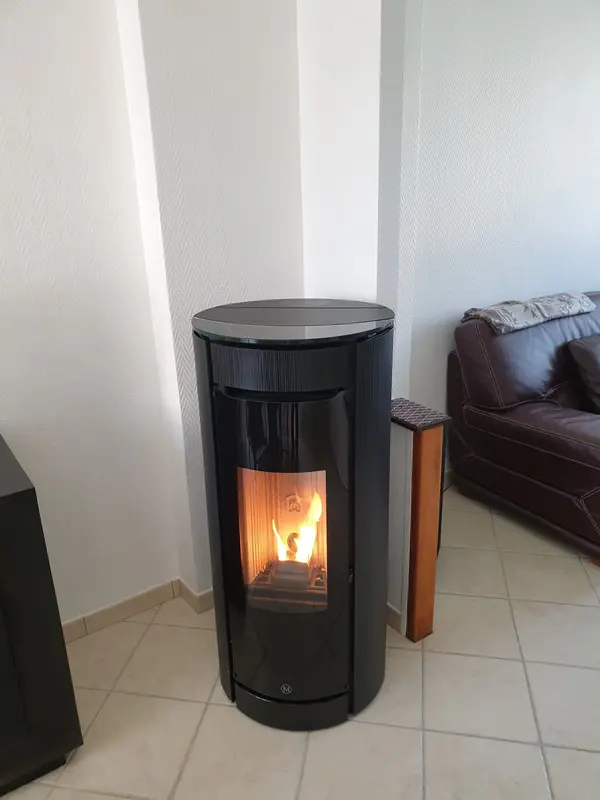 Poêle à granulés rond noir allumé, installé dans l'angle d'un salon carrelé