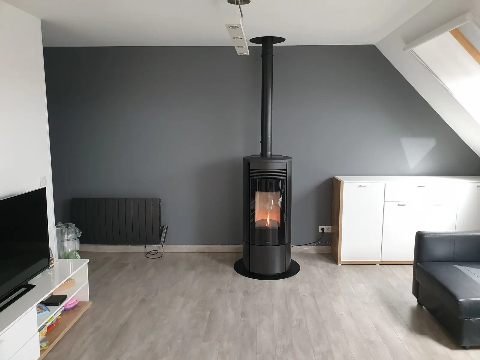Poêle à granulés rond noir installé au centre d'un salon mansardé