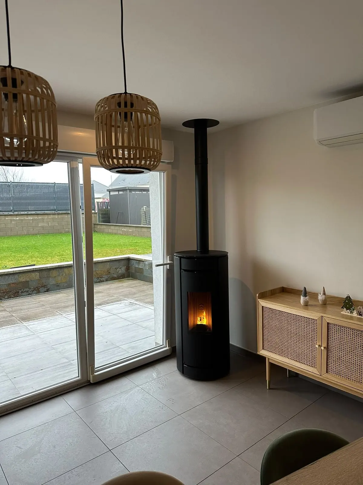 Poêle à granulés noir avec conduit vertical dans un séjour lumineux ouvert sur la terrasse