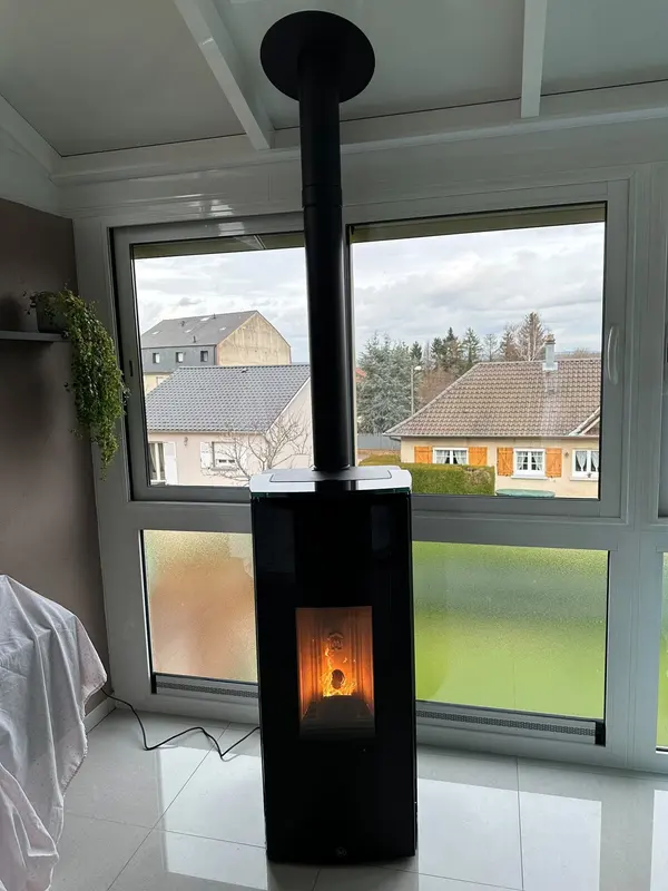 Poêle à granulés noir avec conduit vertical installé devant une grande baie vitrée